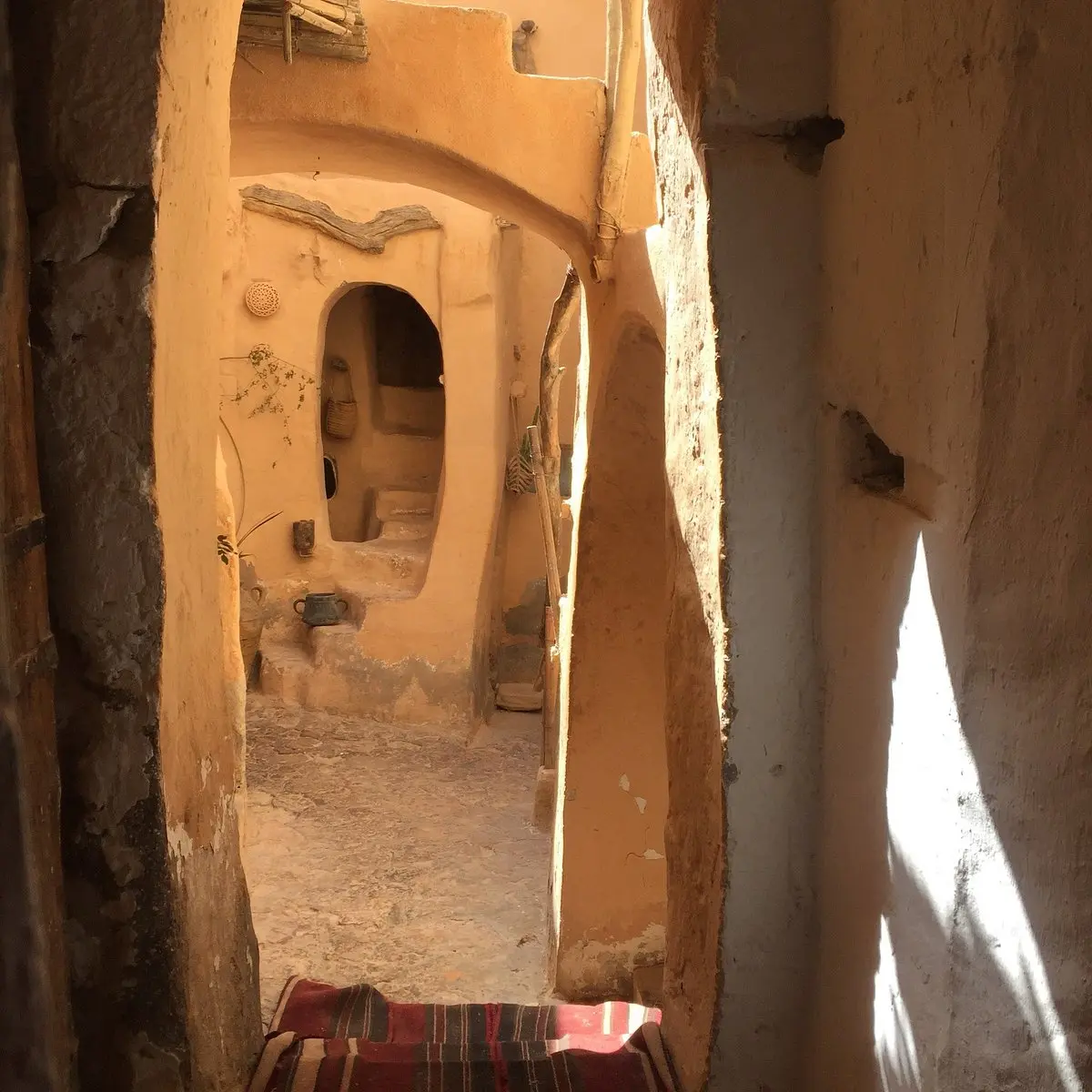 Couloir étroit en architecture traditionnelle de terre crue avec niches murales et lumière naturelle au restaurant Kenza.